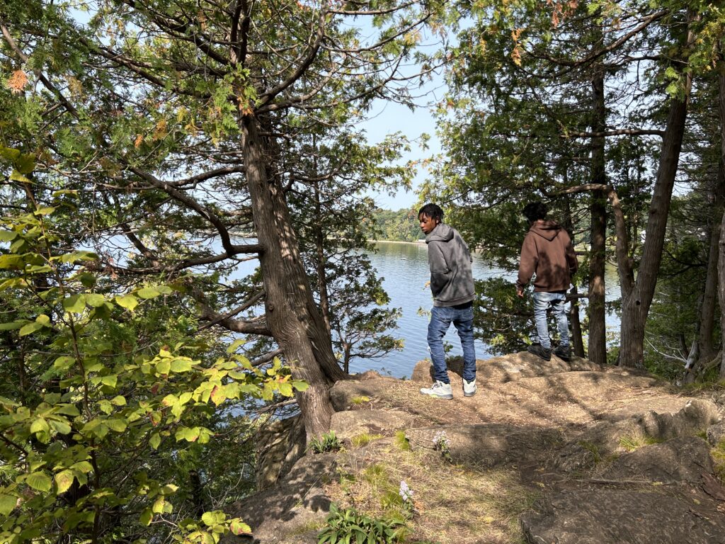 Two boys look over a scenic wooded cliff toward a lake in the distance.