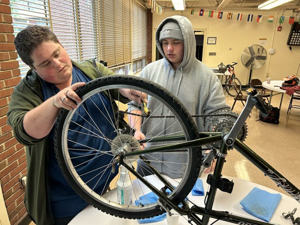 One boy fixing a bicycle chain on a bike while another teenager looks on.