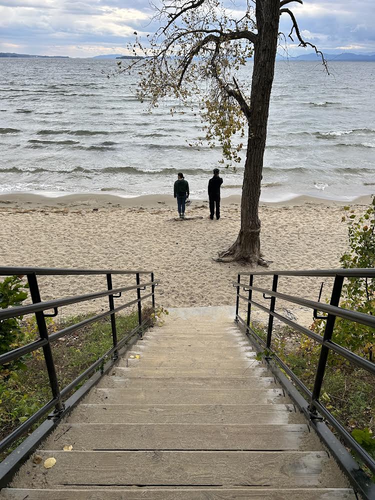 Two people in the far distance, facing away from the camera on a beach by a lake on an autumn day.