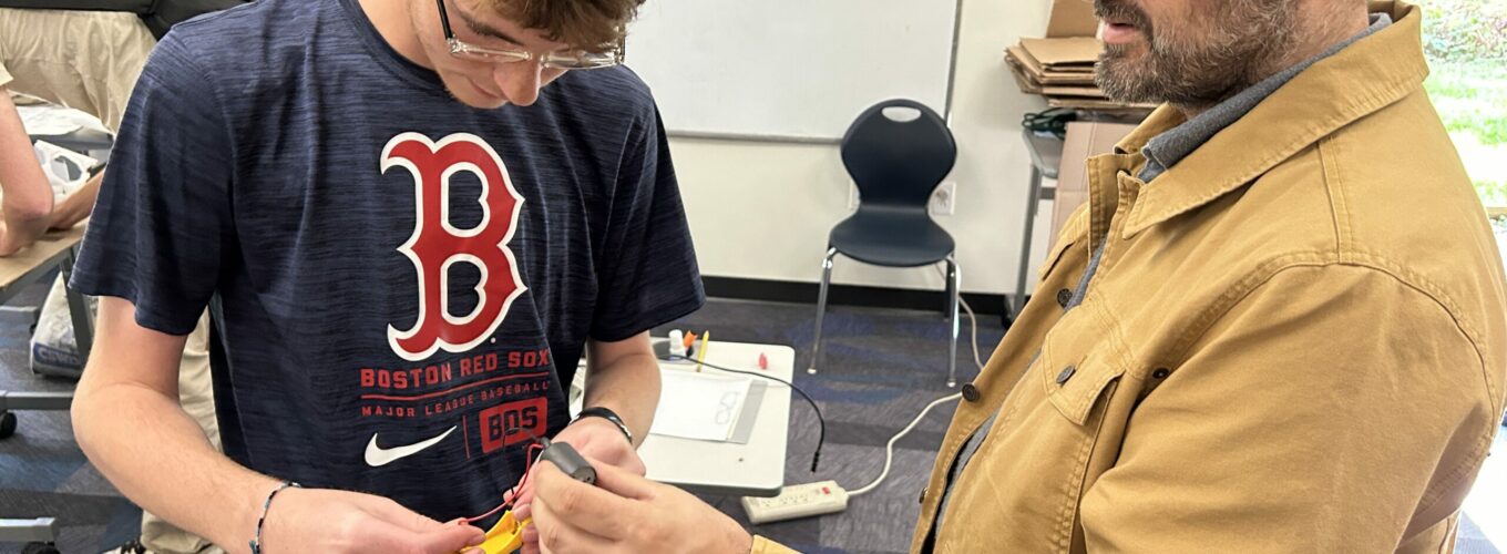 Teacher standing with student as they examine electronic components in the student's hands.