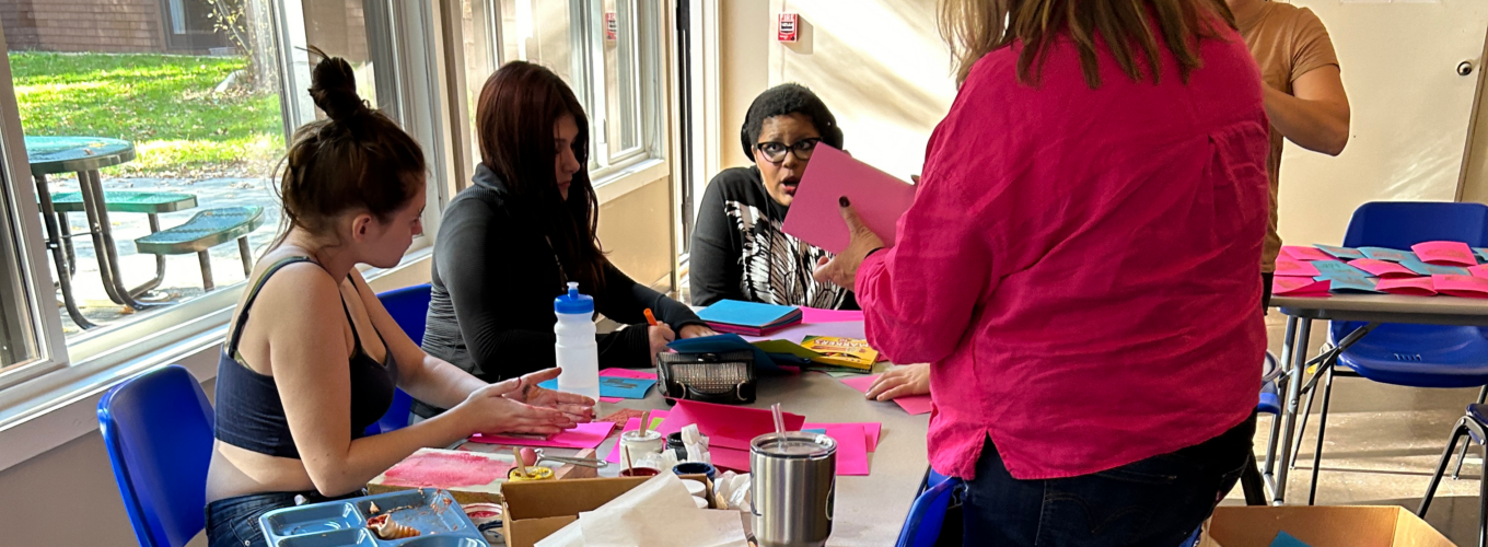 students work on art project as standing teacher looks on.